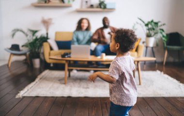 Afro-Amerikalı, hoş kıvırcık saçlı, rahat oturma odasında geniş oturma odasında koşuşturan, farklı ailelerin bulanık arka planlarına karşı...