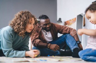 Çok ırklı genç bir çift yerde oturup evde şirin küçük bir çocukla oynuyorlar ve birlikte boş zamanlarını geçiriyorlar.