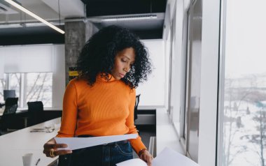 Bir finans müdürü, parlak bir ofis alanındaki karlı zemine karşı sürdürülebilir yatırım stratejisi oluşturan mali belgeleri analiz eder..