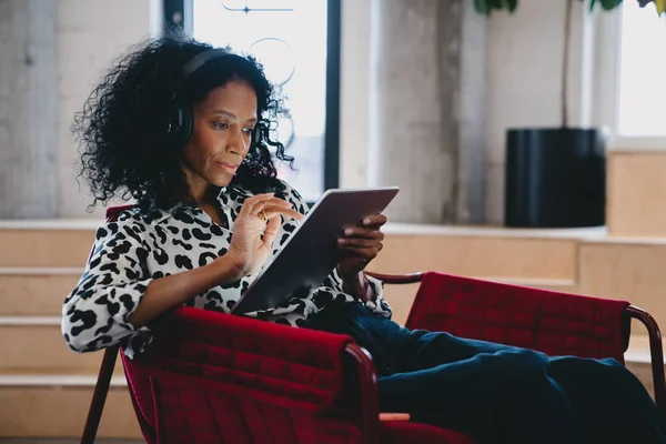 Diligent Black female market analyst in fashion-forward leopard print top, deeply engrossed in financial forecasting on a tablet, in a chic office setting