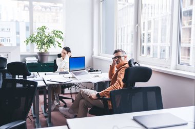 Güncel giysiler içinde düşünceli bir iş adamı, güncel yaratıcı iş yerinde birlikte çalışırken dizüstü bilgisayarının yanında bayan ortağının yanında oturuyor.