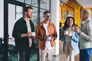 Modern ofiste kahve molası verip eğlendirici deneyimleri dikkatle dinlerken kıdemli bayanlara gülümseyen ve onlara bakan bir grup pozitif çok ırklı iş arkadaşı.