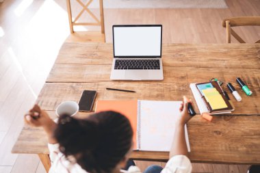 Odaklanmış Afrikalı Amerikalı serbest çalışan, taşınabilir netbook 'lu renkli fosforlu kalemle evden uzakta çalışırken çizim yapan bir kadın.