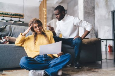 Afro-Amerikalı bir adam genç bir kadınla konuşuyor, modern bir oturma odasında kanepede ve şık bir iç mekanda ilgi ve destek gösteriyor. İlişki sorunu, yanlış anlaşılma yaşayan bir çift.