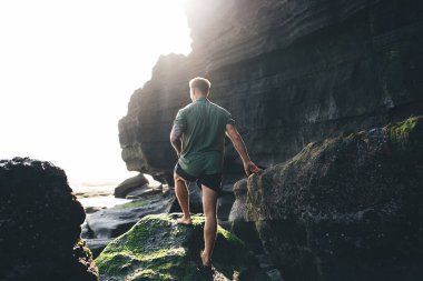 Kayalık kayalıklarda yosunlarla kaplı ve deniz manzarası hayranlık uyandıran gündelik giysiler içinde tanınmayan erkek yolcuların arka plan görüntüsü.