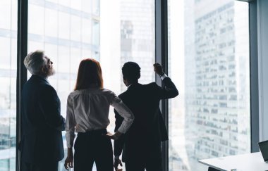 İş merkezinde yeni bir proje üzerinde çalışırken pencerenin yanında duran ve gökdelenleri izleyen tanınmamış çok ırklı iş adamlarının geçmişe bakış