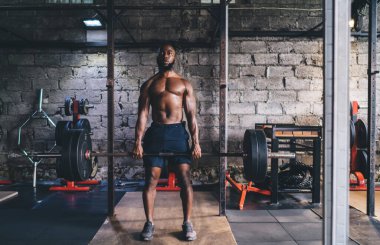 Spor kıyafetleriyle spor yapan formda Afro-Amerikan erkek sporcu halter egzersizi yapıyor beden eğitimi dersinde tuğla duvara karşı ağırlık kaldırıyor ve...