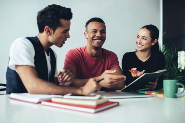 Meslektaşlarıyla işbirliği yaparken gülen, içten gülümseyen neşeli bir adamın portresi. Özel dersten zevk alan mutlu bir grup öğrenci birlikte çalışma alanında öğreniyor.