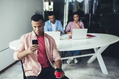 Elinde kafein içeceği olan genç bir adam cep telefonundan iş makalesini kontrol ediyor. İş molasında kahve içmek için 4G kablosuz kullanıyor. Teknoloji ve iletişim kavramı.