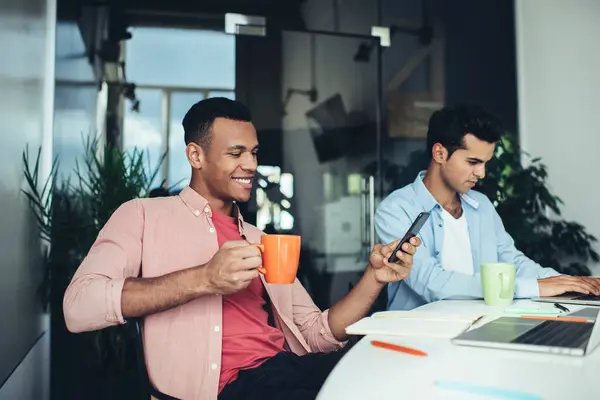 多文化男性同事在与4G无线互联网连接的办公室台式计算机上使用现代技术 微笑的员工通过手机在内容网站上阅读社交新闻 — 图库照片