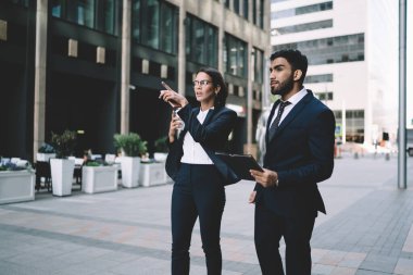 Katı siyah takım elbiseli, odaklanmış çok ırklı iş arkadaşları yazın şehir merkezinde parmaklarını sokakları işaret ederek konuşuyorlar.
