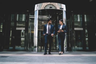 Resmi giyinmiş, gözlüklü, kendine güveni tam bir kadın telefonlu etnik bir erkekle konuşuyor modern ofis binasından ayrılıp birbirlerine bakıyorlar.