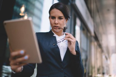Resmi giyinmiş, elinde gözlüklerle çekici bir kadından. Ortağıyla sokakta geçirdiği görüntülü sohbet için tablet kullanıyor.