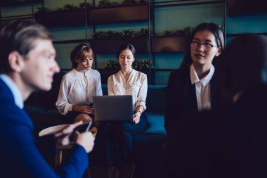 İş merkezinin modern lobisindeki kanepede otururken dizüstü bilgisayarda resmi kıyafet tartışması yapan genç bayan meslektaşlar.  