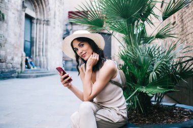 Kameraya bakıp gülümseyen ve elinde akıllı telefonla caddenin ortasında eski binalarla oturan bir kadın.