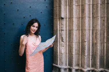 Genç bir kadın gülümseyip kameraya bakarken antik şehir gezisi sırasında tarihi binanın girişini inceliyor.