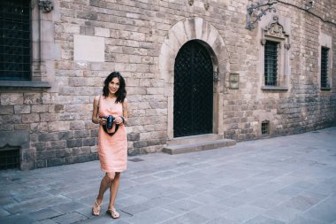 Tam vücut genç bayan gezgin kamerayla gülümsüyor ve antik şehrin sokaklarındaki taş evin dışındaki döküntü kaldırımda duruyor.