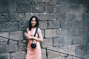 Olumlu kadın fotoğraf makinesiyle gülümseyen ve kameraya bakan yaşlı merdivenlerde duran ve eski püskü taş duvara yaslanan