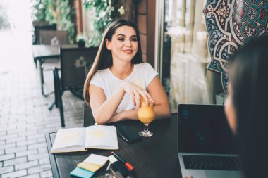 Kendine güveni tam bir kadın, elinde bir bardak meyve suyu defteri ve akıllı telefonla kaldırım kafesinde oturmuş laptopuyla tanınmayan arkadaşını dinliyor.