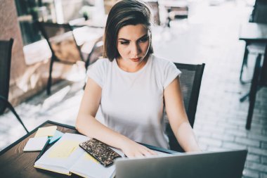 Kafe terasındaki projede çalışırken dizüstü bilgisayarı dikkatle izleyen zeki ve konsantre genç bir bayandan.