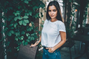 Gündelik beyaz gömlekli, kot pantolonlu, kafeterya terasında el ele duran ve hafif gülüşlü kameraya bakan kendine güvenen modern esmer.