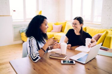 Siyahtan esinlenilmiş bir kadının siyah elbiseli arkadaşına tek kullanımlık fincanda kahve içerken gülümsemesi.