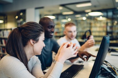 Tek bir bilgisayarda birlikte çalışan ve ortak proje planını tartışırken ekranı işaret eden çok ırklı ve aktif öğrencilerin yan görünümü