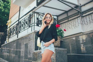 Şehir caddesinde cep telefonuyla konuşurken gülümseyen ve kameraya bakan modaya uygun giyinen sarı saçlı hoş bayandan. 