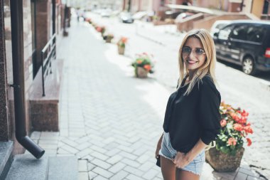 Modern şehir caddesine gülümseyen ve kameraya bakan, modaya uygun giyinmiş, sarı saçlı, genç bir bayandan.