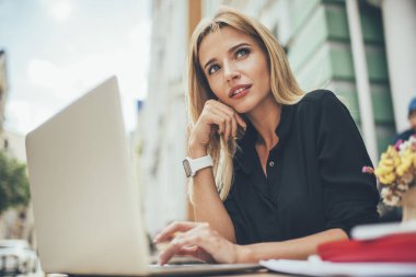 Düşünceli, çekici, gündelik giyinmiş genç bir kadının dizüstü bilgisayarını kullanarak sokak kafesinde bilgisayar başında çalışıp gözlerini başka yöne çevirmesinden.