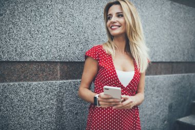 Kırmızı benekli elbiseli, kendine güvenen genç bir bayan modern şehrin sokaklarında sosyal medyada sohbet ediyor.