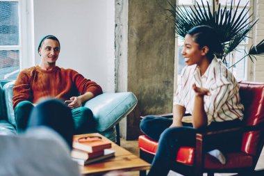 Çizgili tişörtlü, neşeli Afrikalı Amerikalı kadının yandan görünüşü canlı, şık bir adam ise düşünceli bir şekilde odayı dinliyor.