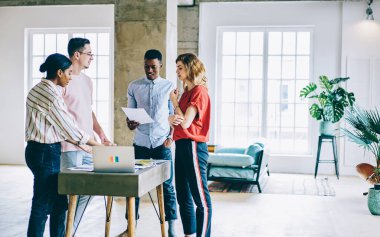 Gülümseyen zeki, zeki, çok ırklı iş arkadaşları gündelik giysiler içinde modern aydınlık ofis alanındaki masada duran belgeleri kontrol ediyorlar.