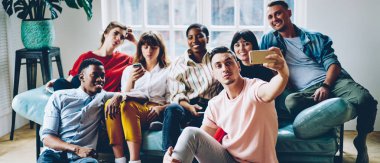 Milenyum çağının neşeli, çok ırklı öğrencilerinin çağdaş dairede boş zamanlarında akıllı telefonlarıyla selfie çekmeleri.