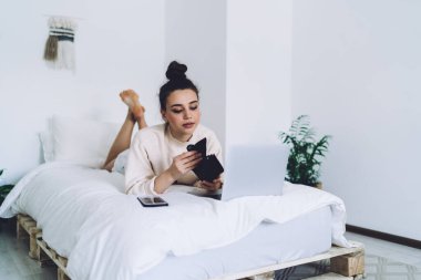 Çıplak ayaklı, tüylü, rahat beyaz bir yatakta dizüstü bilgisayarı ve aleti olan bir kadın sabahları evde tek başına vakit geçiriyor.