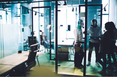 Resmi olarak kadın ve erkek çalışanlar, modern ofiste cam arkasında şirket stratejisini tartışan belgeler taşıyorlar.