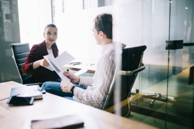 Saygın girişimci elinde belgelerle parlak bir ofiste oturuyor ve kadın iş ortağıyla ortak projenin detaylarını tartışıyor.