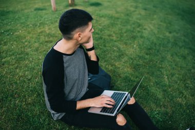 Şehirdeki yeşil çimlerde oturup dizüstü bilgisayarda interneti karıştıran sıradan bir adamın bakışları.