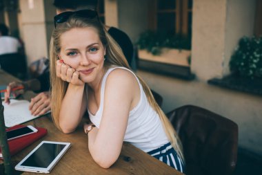 Beyaz kolsuz tişörtlü gülümseyen modern bayan öğrenci masada boş siyah ekranlı tabletle otururken grup arkadaşıyla buluşuyor ve ev ödevlerine yardım ediyor.