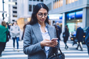 Gündüz vakti New York 'ta karşıdan karşıya geçerken cep telefonu kullanan gömlek ve gri ceket giyen çekici genç bir iş kadını.