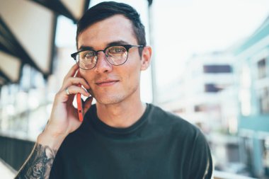 Gözlüklü yakışıklı hippinin yakın plan portresi cep telefonu uygulaması üzerinden arkadaşıyla iletişim kurarken kameraya bakıyor, beyaz bir genç uluslararası konuşma yapıyor.