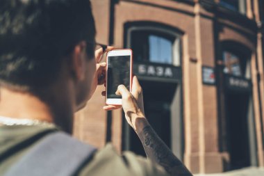 Arka planda boş ekran cep telefonuyla fotoğraf çeken erkek turistin tuğladan yapılmış modern binası bulanık arka planda. 