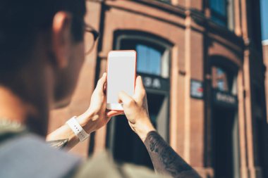 Çevrimiçi uygulamaya bağlı şehir ortamında bina resimleri yapan bin yıllık hipster gezgininin kırpılmış resmi ve medya yayınları için 4g İnternet, cep telefonu üzerine seçici odaklanma