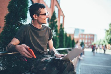 Gözlüklü, gülümseyen, serbest çalışan, temiz hava alan, akıllı telefon cihazlı başarılı hippi, internet sitesinde yayınlanan komik bilgilerle gülüyor.