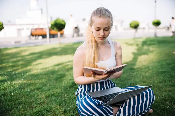 Şehirdeki yeşil çimlerde dizlerinin üstüne çöküp haftanın günlüğünü kontrol eden ciddi konsantre kadın serbest yazar.