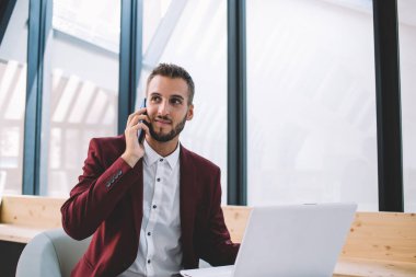 Modern ofiste cep telefonuyla iş arkadaşıyla iletişim kuran, dizüstü bilgisayar kullanan, resmi giyinmiş, zeki bir erkek.