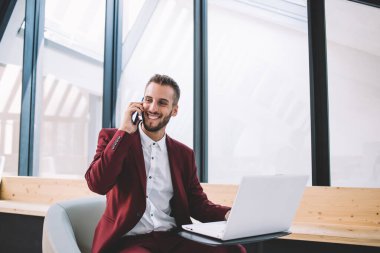 Zarif takım elbiseli, gülümseyen etnik adam modern ofis alanındaki masada oturan cep telefonu kullanarak projenin başarısını tartıştığına sevindim. 