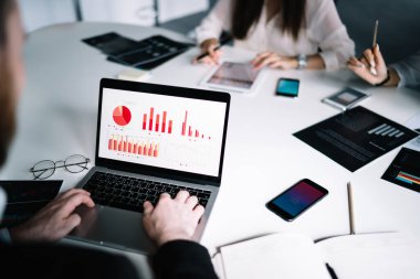 Renkli diyagramları ve istatistikleri inceleyen dizüstü bilgisayar kullanan resmi erkek çalışanı akıllı telefonun yanında kadınlarla masaya oturtun