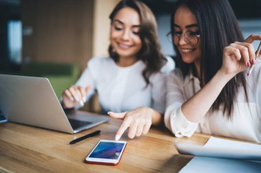 Şık giyinmiş, gülümseyen ve modern akıllı telefonları kullanan genç kadınlar masa başında dinleniyorlar.