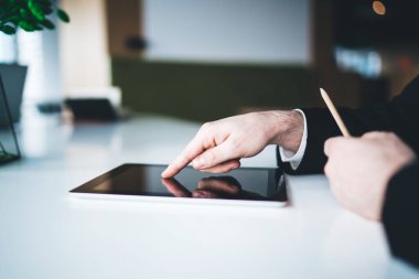 Takım elbiseli genç bir erkek ofis çalışanının gün ışığında şehir ofisindeki masada otururken tablet üzerinde gezinirken görüntüsü